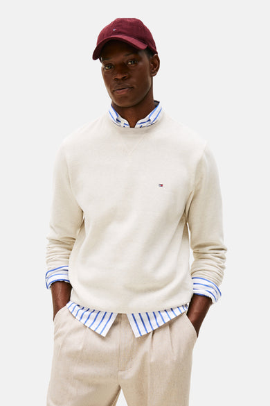 Ecru ronde hals sweatshirt van Tommy Hilfiger, gedragen over een gestreept overhemd, met een beige broek en een bordeauxrode pet.