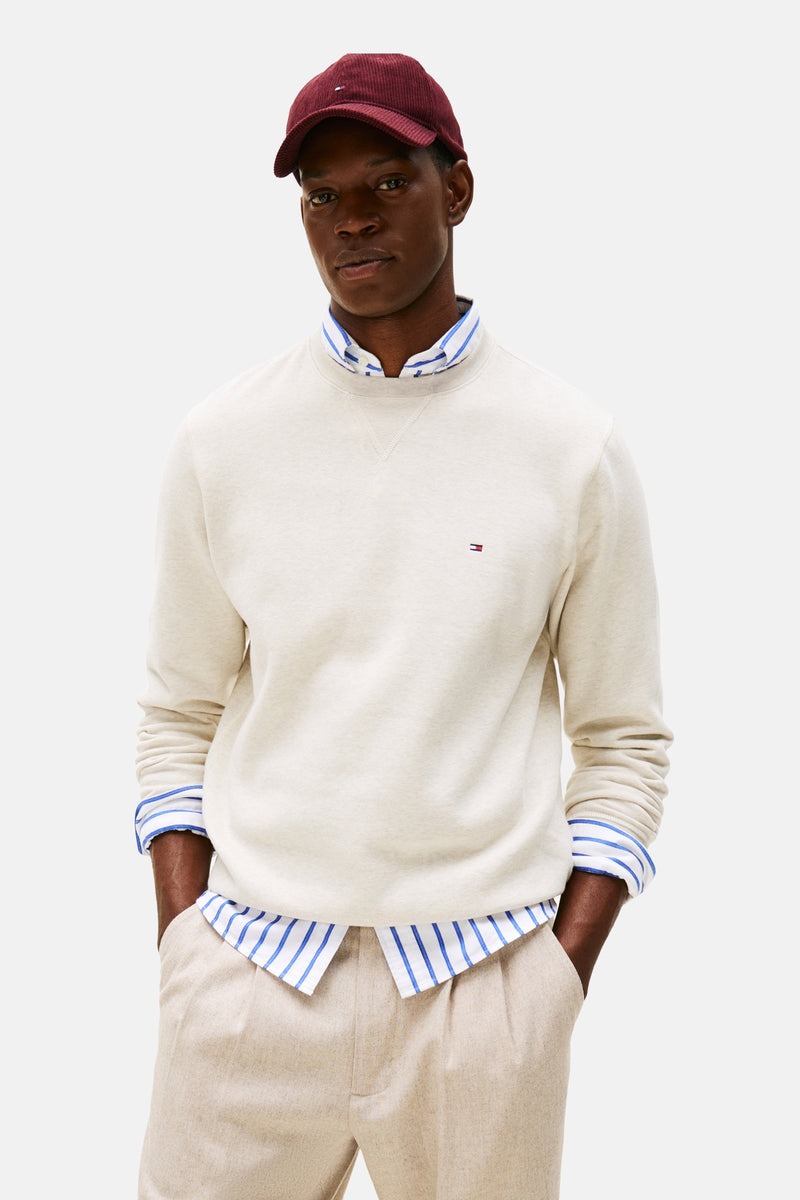 Ecru ronde hals sweatshirt van Tommy Hilfiger, gedragen over een gestreept overhemd, met een beige broek en een bordeauxrode pet.