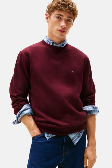 Rode ronde hals sweatshirt van Tommy Hilfiger, gedragen over een blauw geruit overhemd en donkere jeans.
