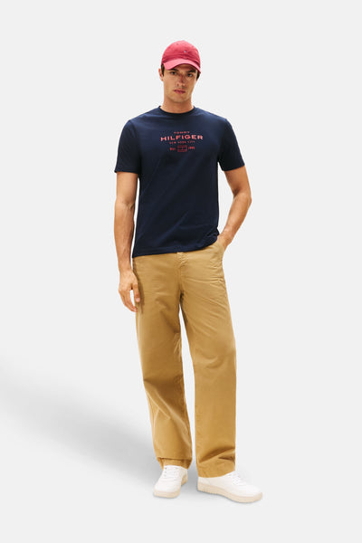 Marineblaues T-Shirt mit kurzen Ärmeln von TOMMY HILFIGER, getragen mit einer beigen Hose und einer roten Kappe.