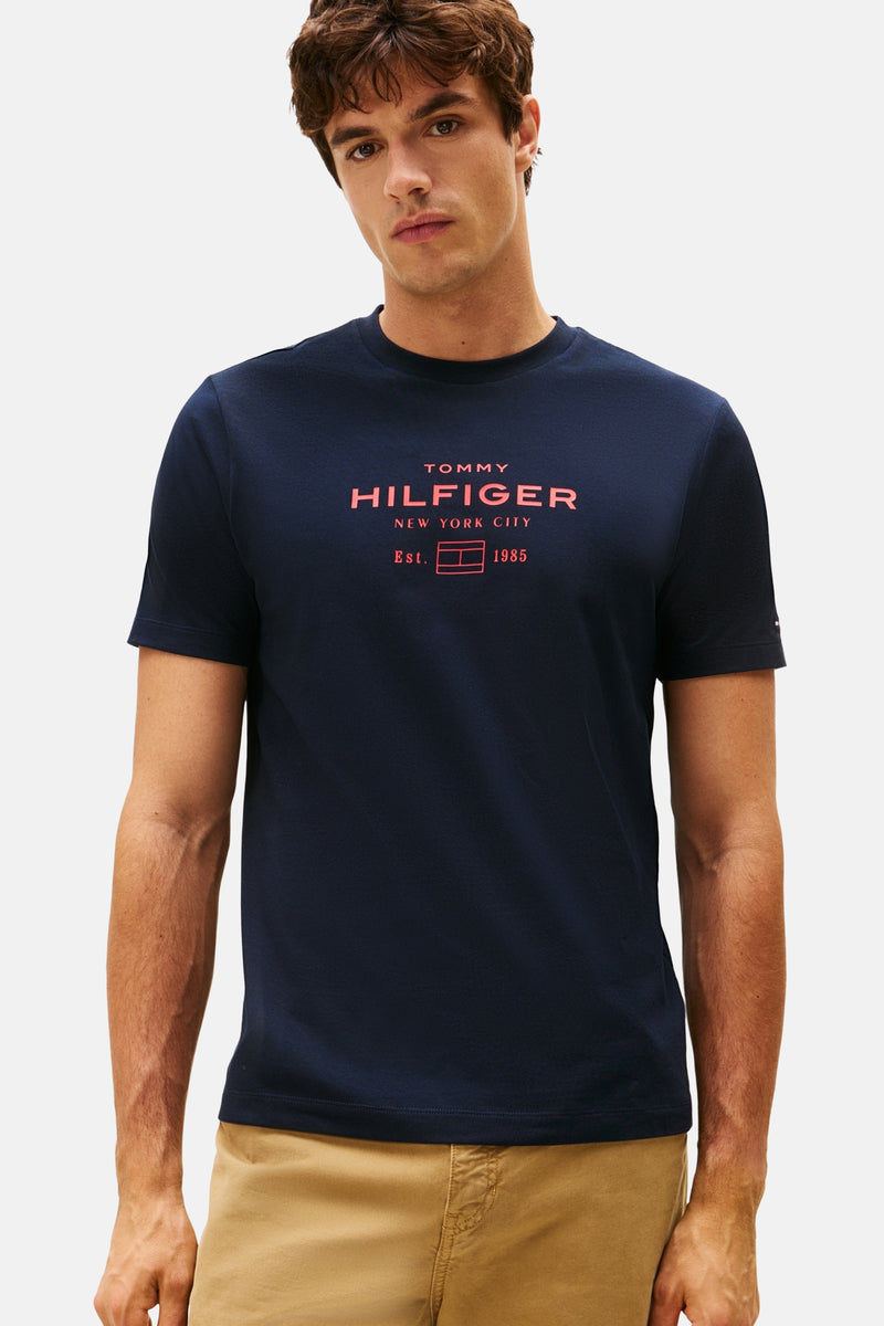 Blauw T-shirt met korte mouwen van TOMMY HILFIGER met rode opdruk op de voorkant, gedragen met een kaki broek.