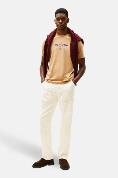 Beige T-shirt met korte mouwen van TOMMY HILFIGER, gedragen met een bordeauxrode trui over de schouders en een witte broek.
