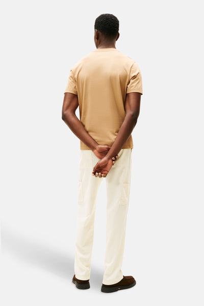 Beige T-shirt met korte mouwen van Tommy Hilfiger, gedragen met een lichte broek en bruine schoenen, achtergezicht.