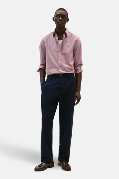 Rood geruit overhemd met lange mouwen van TOMMY HILFIGER, open gedragen over een wit T-shirt, met een marineblauwe broek en loafers.