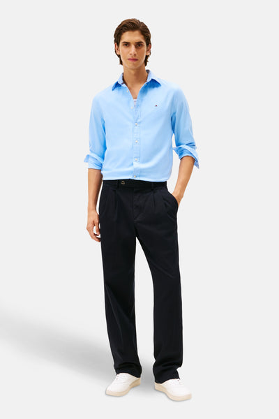 Chemise à manches longues bleue de TOMMY HILFIGER, portée avec un pantalon noir et des chaussures blanches.