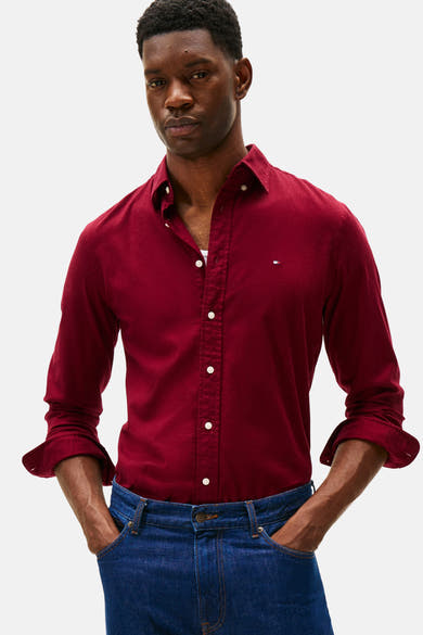 Chemise bordeaux à manches longues de Tommy Hilfiger, portée avec un jean bleu, les mains dans les poches.
