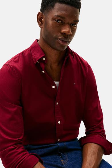 Chemise bordeaux à manches longues de TOMMY HILFIGER, partiellement boutonnée, portée avec un débardeur blanc et un jean bleu foncé.