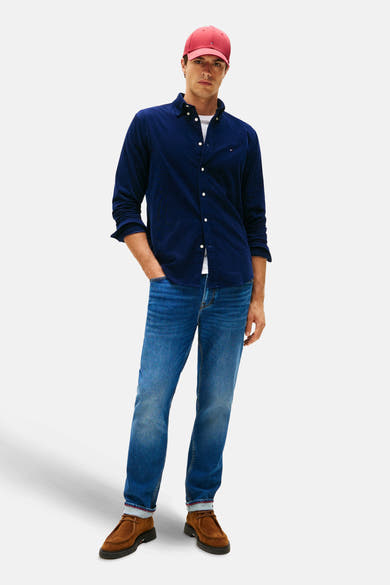 Blauwe Tommy Hilfiger corduroy overhemd, open gedragen over een wit T-shirt, met een spijkerbroek en een rode pet.