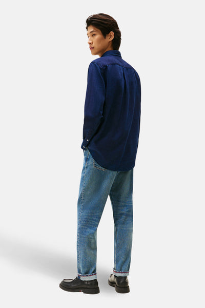 Chemise à manches longues bleue de TOMMY HILFIGER portée avec un jean et des chaussures noires, vue de dos.

