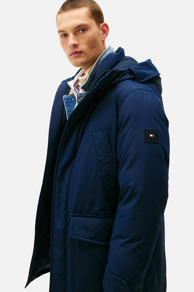 Imperméable bleu de TOMMY HILFIGER avec capuche, porté sur une veste en jean et un pull rayé