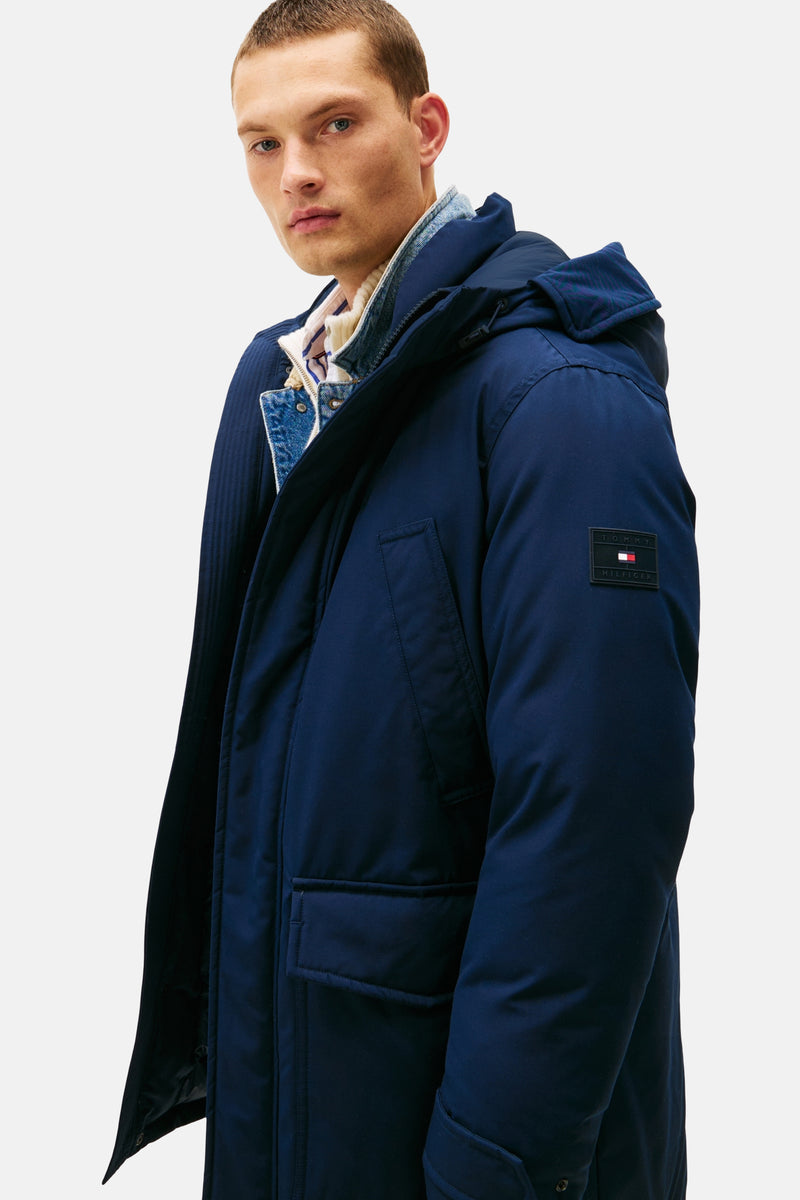 Imperméable bleu de TOMMY HILFIGER avec capuche, porté sur une veste en jean et un pull rayé