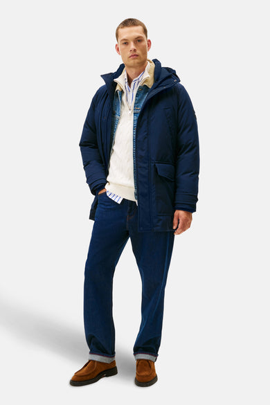 Veste de pluie bleue de TOMMY HILFIGER, portée avec un pull blanc, une chemise rayée et un jean foncé.