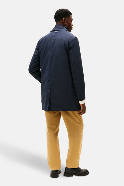 Veste longue bleue par TOMMY HILFIGER, vue de dos, portée avec un pantalon beige et des mocassins noirs.