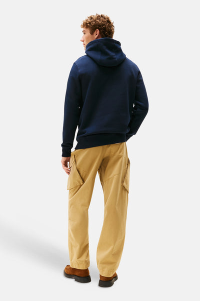 Marineblauwe hoodie van TOMMY HILFIGER, gedragen met een beige cargobroek en bruine schoenen, achterzijde.