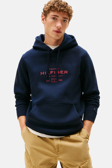 Marineblauwe hoodie van Tommy Hilfiger met rood logo en een beige broek.