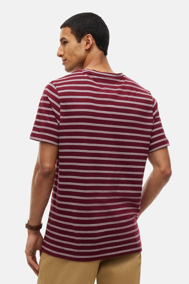 Burgundy short-sleeve t-shirt with white horizontal stripes, back view, worn with beige pants and brown leather watch.