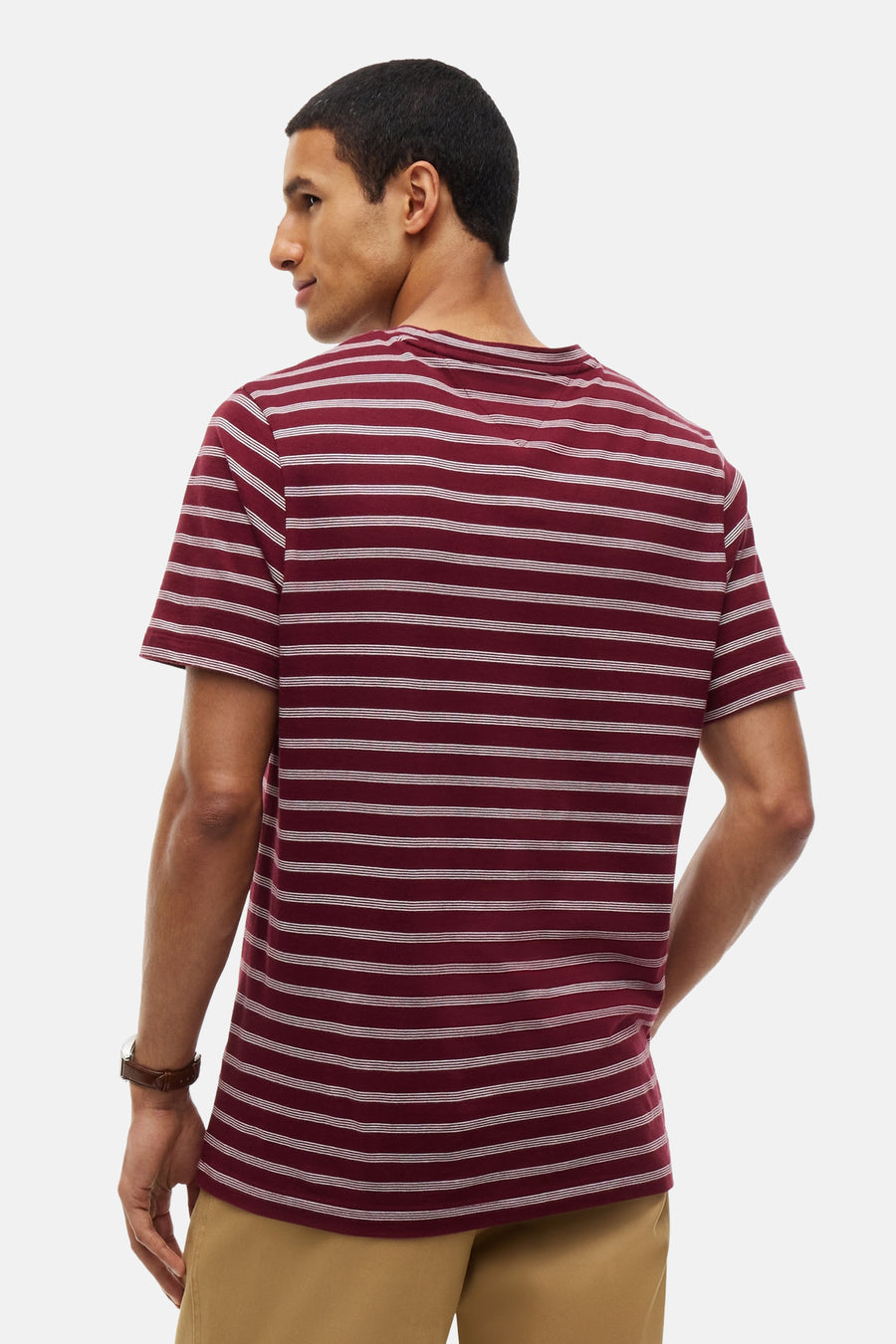 Burgundy short-sleeve t-shirt with white horizontal stripes, back view, worn with beige pants and brown leather watch.