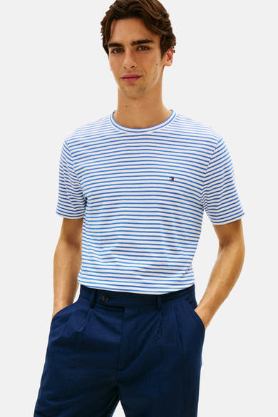 T-shirt bleu à rayures, de Tommy Hilfiger, avec un logo discret sur la poitrine, porté avec un pantalon bleu marine.