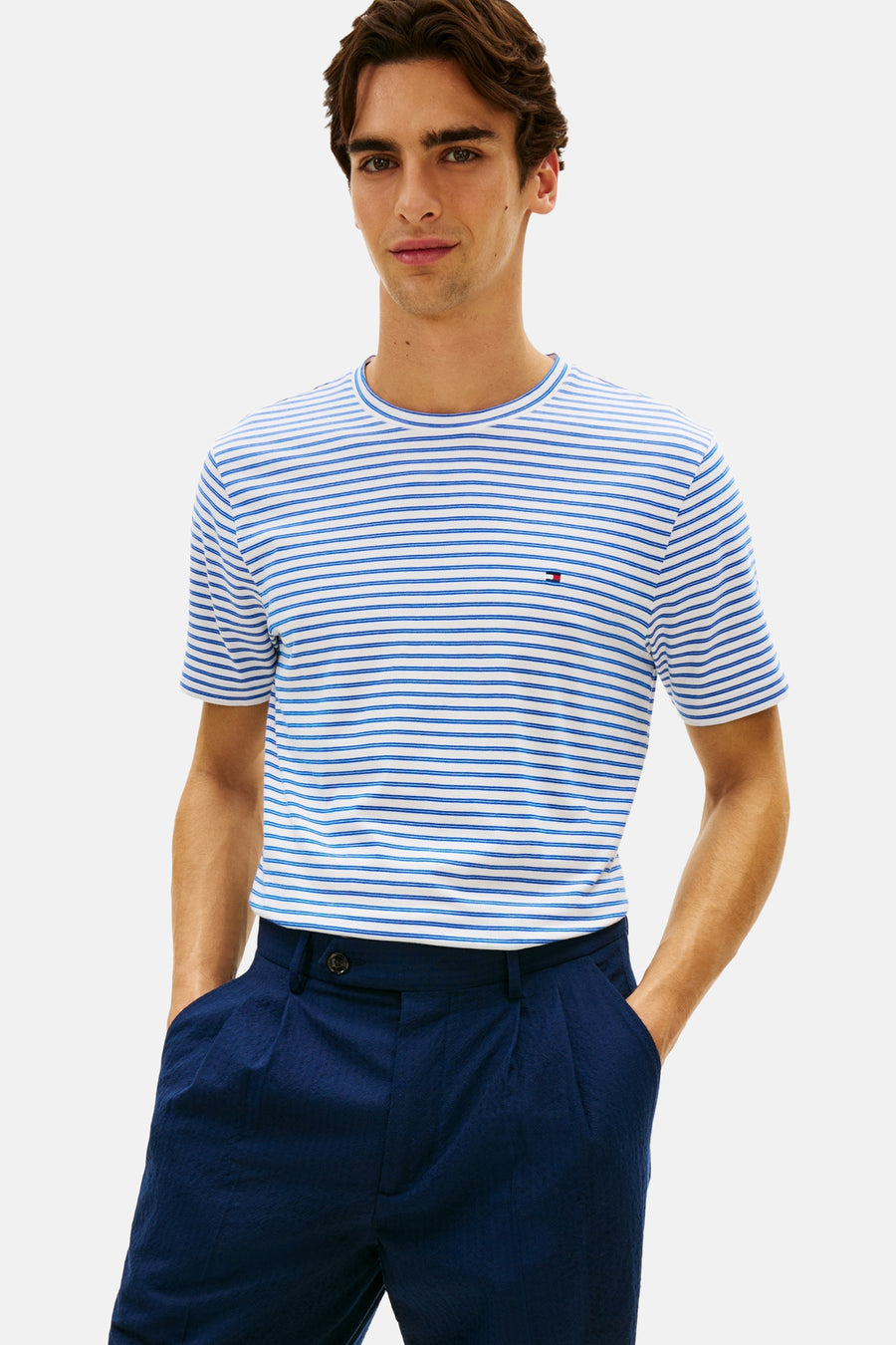 T-shirt bleu à rayures, de Tommy Hilfiger, avec un logo discret sur la poitrine, porté avec un pantalon bleu marine.