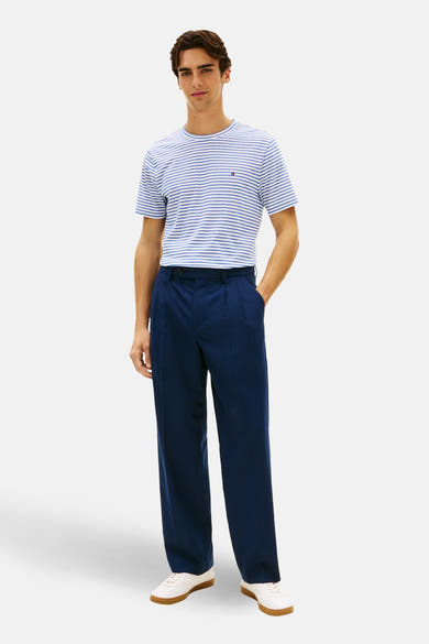 T-shirt à manches courtes bleu rayé de TOMMY HILFIGER, porté avec un pantalon marine et des baskets blanches.