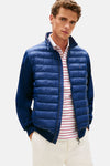 Veste bleu de TOMMY HILFIGER, style bomber, manches longues bleu marine, portée sur un polo rayé rouge et blanc.