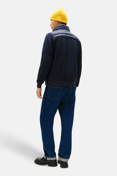 Blauwe jas van TOMMY HILFIGER, met gewatteerd inzetstuk en man die een gele muts en een blauwe spijkerbroek draagt.