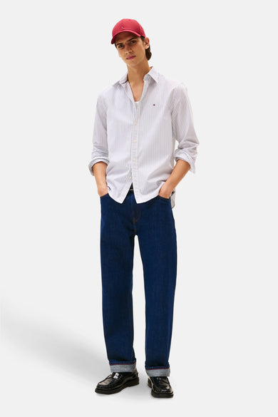 Wit gestreept overhemd met lange mouwen van TOMMY HILFIGER, gedragen met een donkerblauwe spijkerbroek en een rode pet.