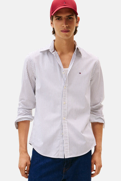 Wit gestreept overhemd met lange mouwen van TOMMY HILFIGER, gedragen met een wit T-shirt en een rode pet.