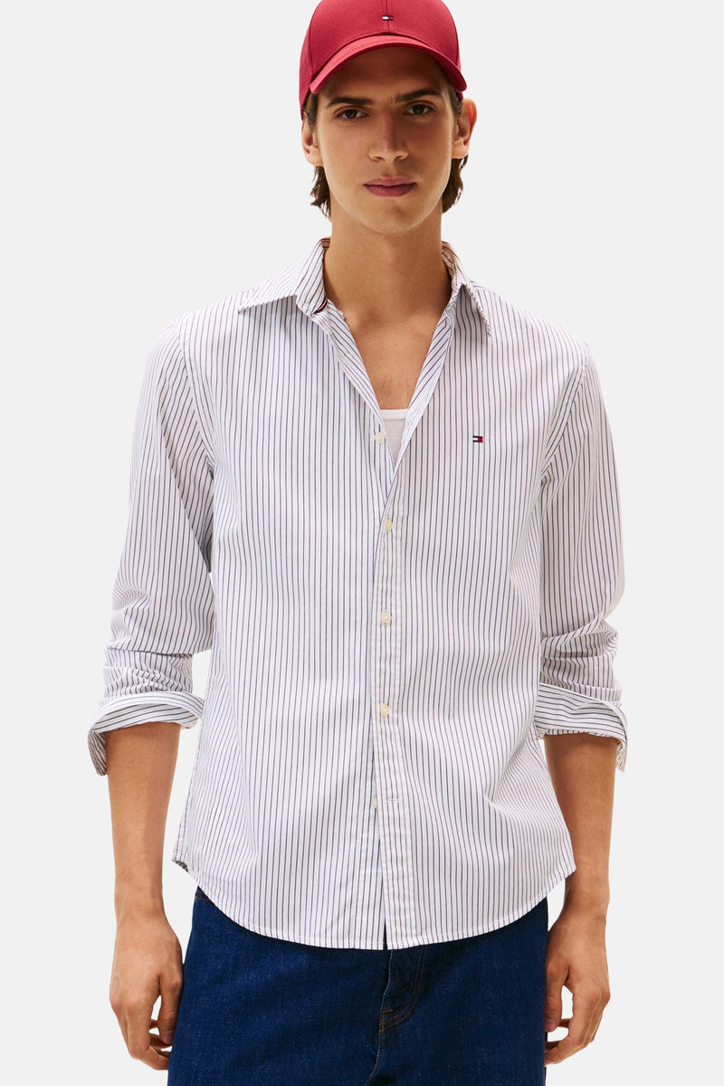 Wit gestreept overhemd met lange mouwen van TOMMY HILFIGER, gedragen met een wit T-shirt en een rode pet.