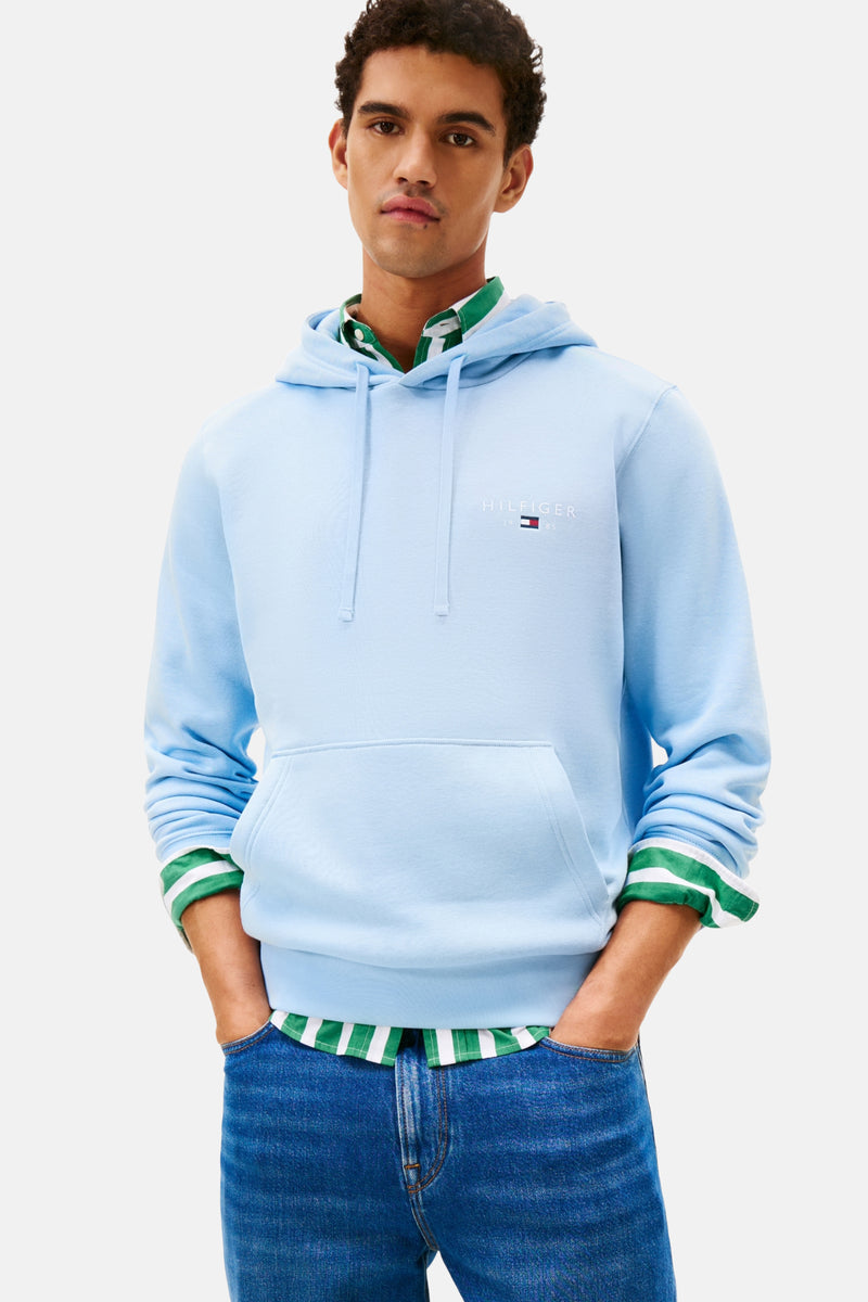 Blauwe hoodie van TOMMY HILFIGER, gedragen met een groen-wit gestreept overhemd en een spijkerbroek.
