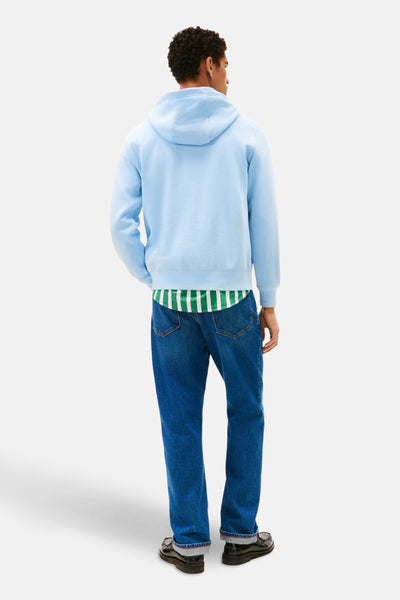 Sweat à capuche bleu de TOMMY HILFIGER, porté avec une chemise rayée verte et blanche et un jean bleu.