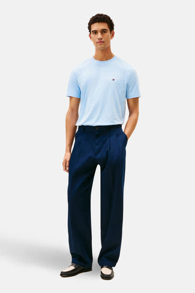 T-shirt bleu à manches courtes de TOMMY HILFIGER, porté avec un pantalon bleu marine à plis et des mocassins en cuir noir et crème.