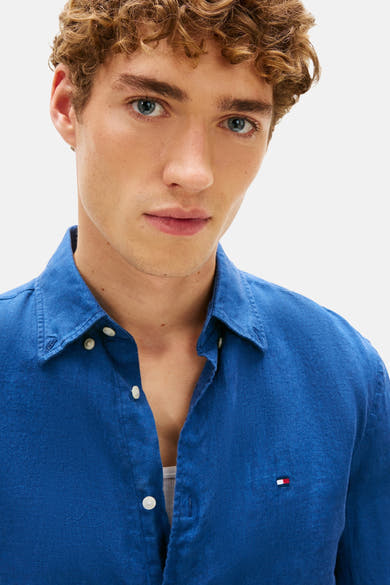 Blauw overhemd met lange mouwen van Tommy Hilfiger, logodetail op de borst, gedragen open over een witte tanktop.