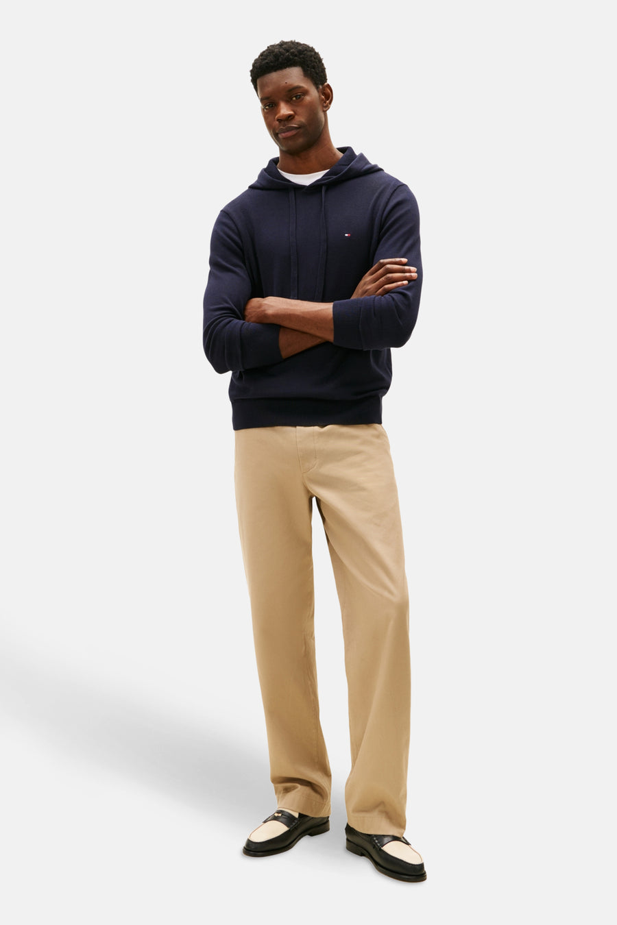 Sweat à capuche bleu par Tommy Hilfiger, porté avec un t-shirt blanc et un pantalon beige.