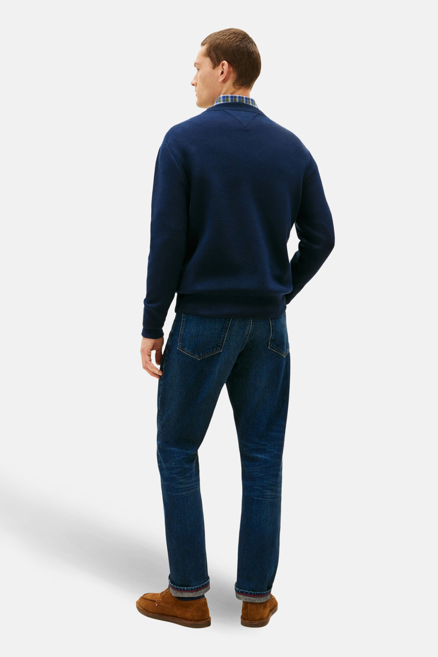 Pull à col rond bleu de TOMMY HILFIGER, porté avec une chemise à carreaux et un jean bleu foncé.