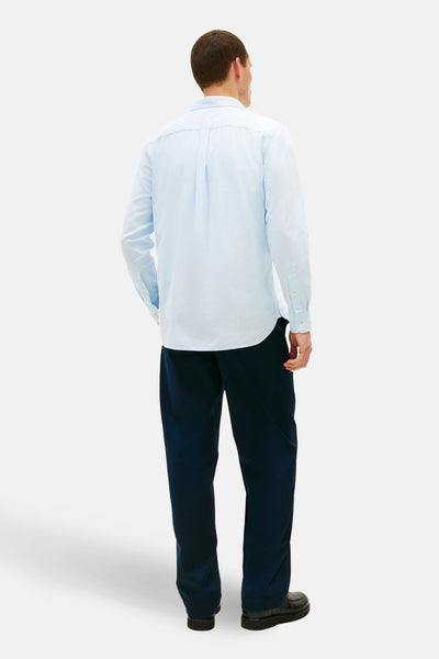 Chemise à manches longues bleue de TOMMY HILFIGER, avec boutons et pli au dos, portée avec un pantalon sombre.