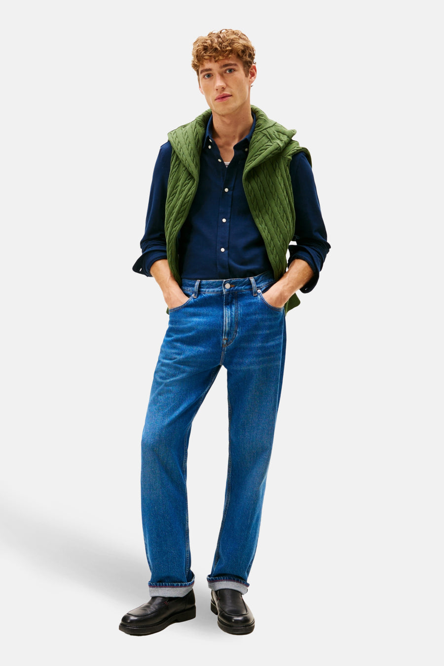 Chemise à manches longues bleue de Tommy Hilfiger, portée avec un gilet vert en maille torsadée et un jean.
