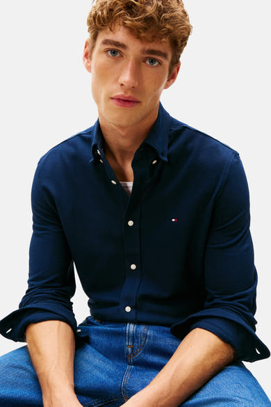 Chemise à manches longues bleue de TOMMY HILFIGER, portée avec un jean, modèle masculin aux cheveux bouclés.
