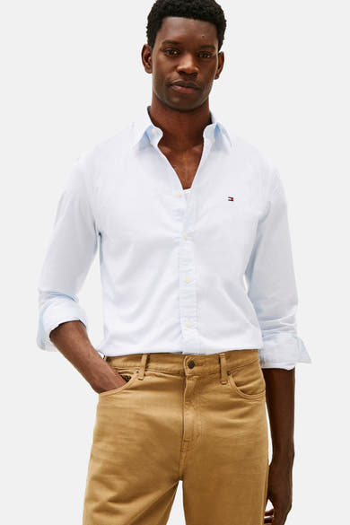 Chemise à manches longues bleue de TOMMY HILFIGER, à motif discret, portée avec un pantalon chino marron.