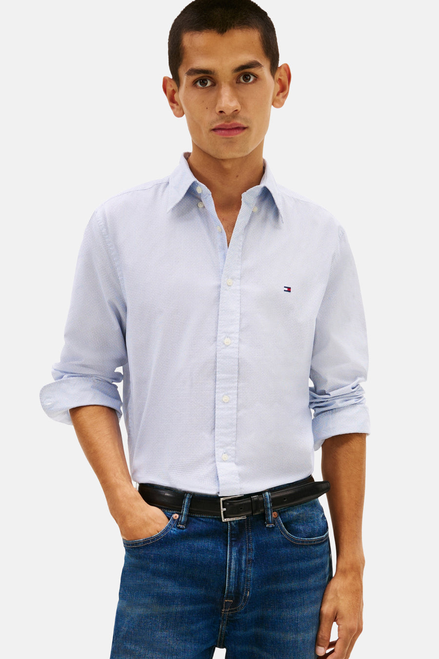 Chemise à manches longues bleue de TOMMY HILFIGER, motif discret, portée avec un jean bleu et une ceinture noire.
