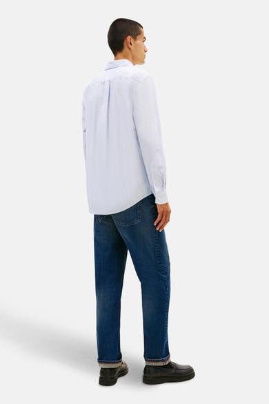 Chemise à manches longues bleue de TOMMY HILFIGER, vue de dos, portée avec un jean bleu et des mocassins noirs.