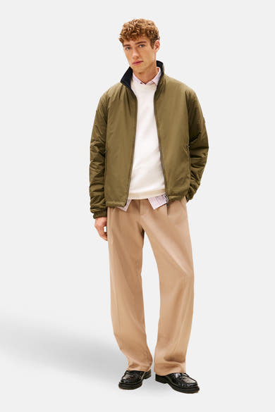 Veste de pluie kaki par Tommy Hilfiger, portée avec un pull blanc et un pantalon beige ample.