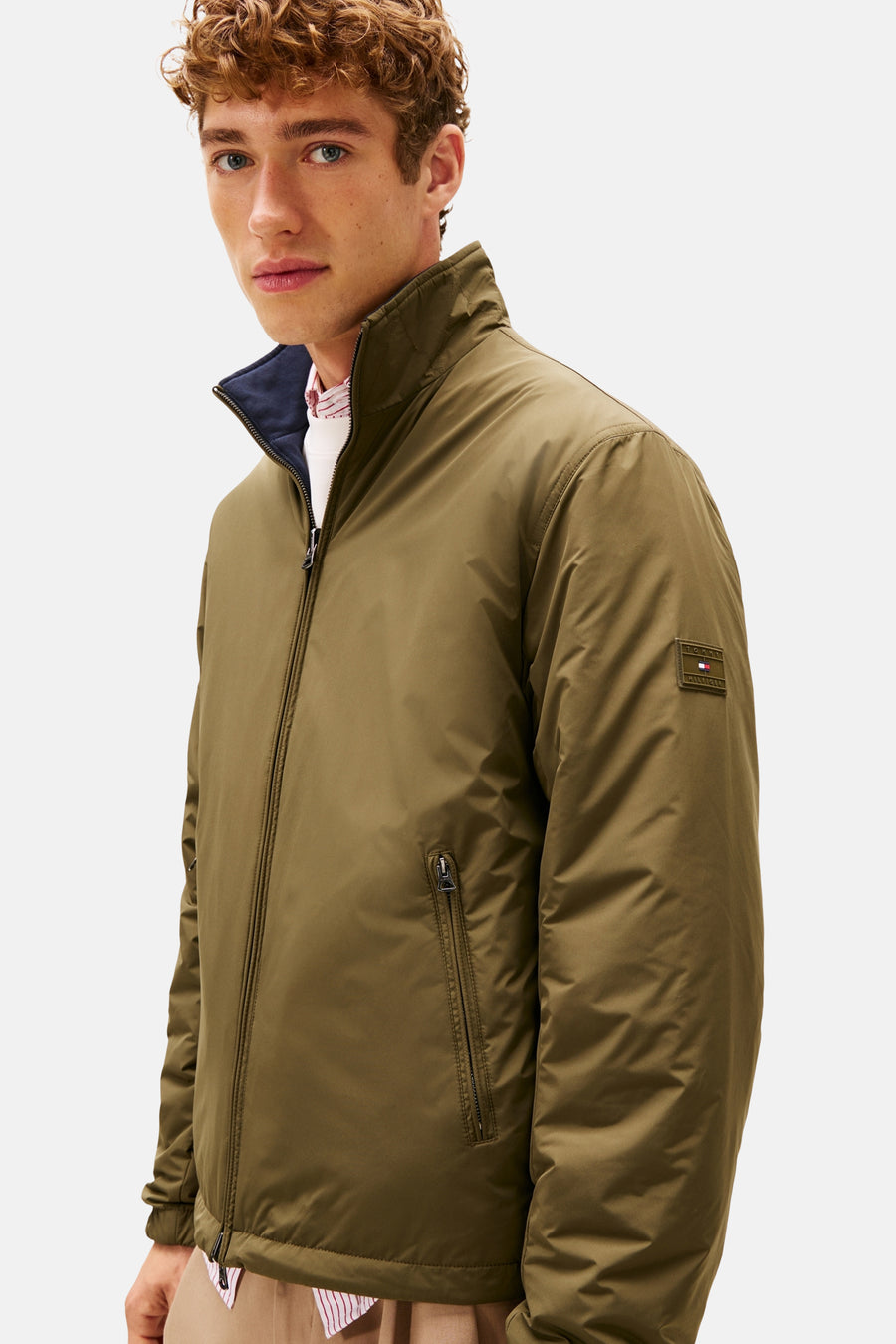 Kaki regenjas van TOMMY HILFIGER, met ritssluiting en zak met rits, gedragen over een gestreept overhemd.