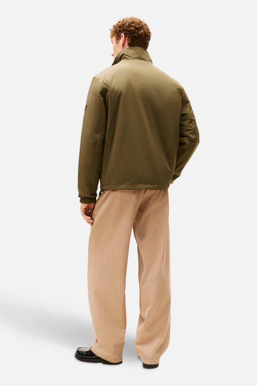 Kaki regenjas van TOMMY HILFIGER, van achteren gezien, met een wijde beige broek en zwarte schoenen.