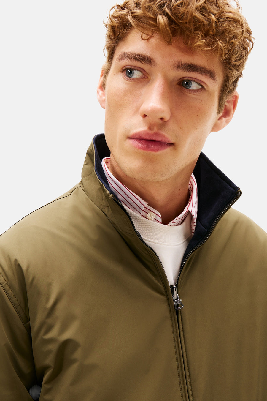 Kaki regenjas van TOMMY HILFIGER met opstaande kraag, gedragen over een witte trui en een gestreept overhemd.