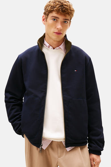 Kaki regenjas van Tommy Hilfiger met ritssluiting en zakken, gedragen met een gestreept overhemd en een witte trui.