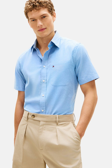 Chemise à manches courtes bleue de TOMMY HILFIGER, avec poche poitrine et pantalon beige à plis.
