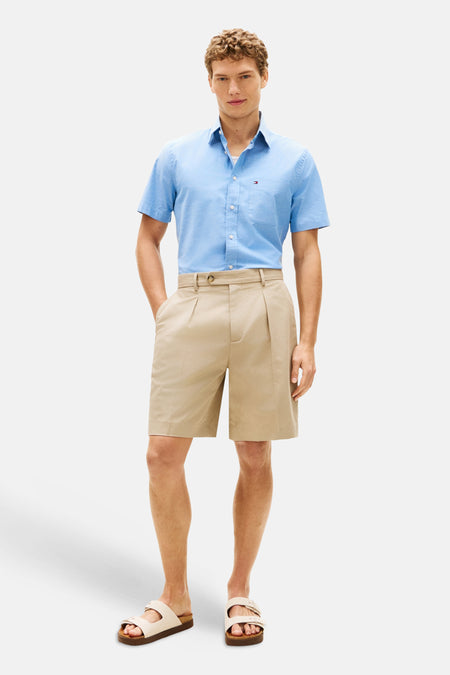 Chemise à manches courtes bleue de Tommy Hilfiger avec un logo subtil sur la poitrine, portée avec un short beige et des sandales.