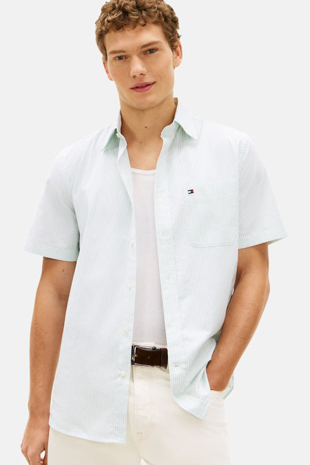 Chemise à rayures blanches à manches courtes de Tommy Hilfiger, portée sur un débardeur blanc avec une ceinture en cuir marron