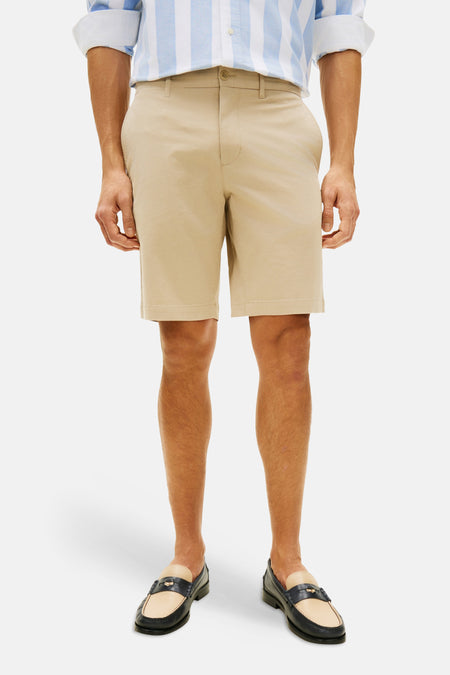 Beige Bermuda van Tommy Hilfiger, gedragen met een blauw-wit gestreept overhemd en loafers.